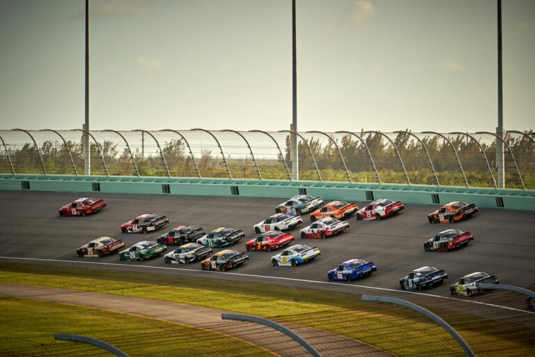 High-speed NASCAR race featuring multiple cars on a sunny day in Miami.
